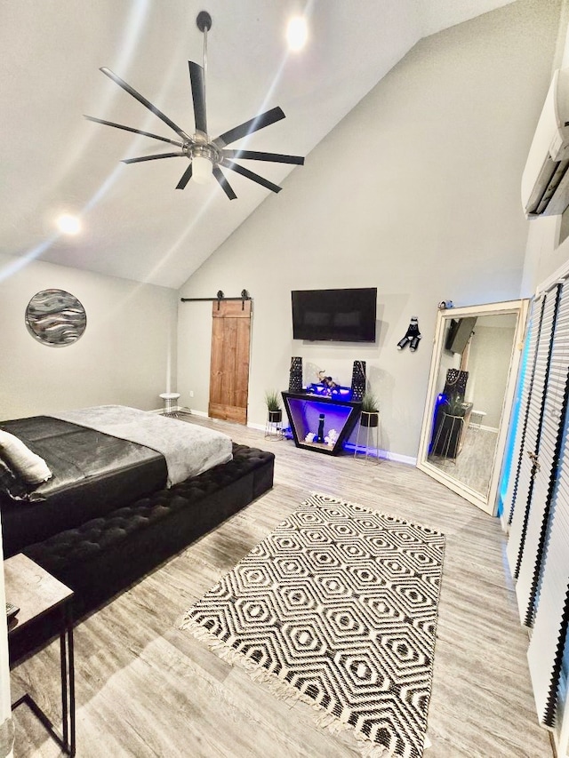 bedroom featuring high vaulted ceiling, a barn door, light wood-type flooring, ceiling fan, and a wall mounted AC