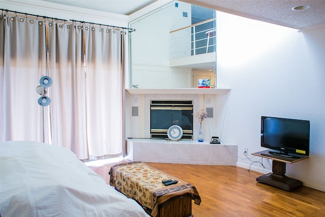 bedroom featuring wood-type flooring, a textured ceiling, a fireplace, and crown molding