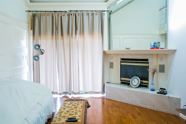 bedroom featuring ornamental molding, a tiled fireplace, and hardwood / wood-style flooring