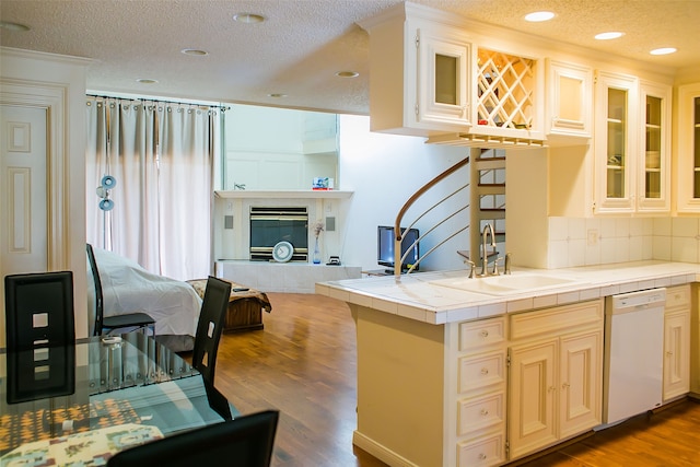 kitchen featuring wood-type flooring, tile counters, sink, a fireplace, and white dishwasher