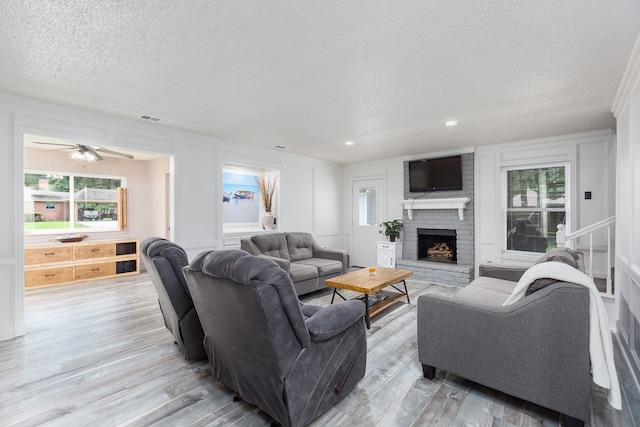 living room featuring a brick fireplace, a textured ceiling, light hardwood / wood-style floors, and ceiling fan