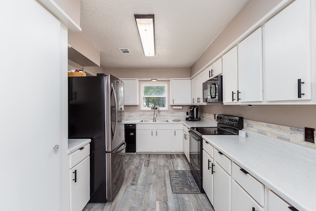 kitchen with white cabinets, a textured ceiling, black appliances, light hardwood / wood-style floors, and sink