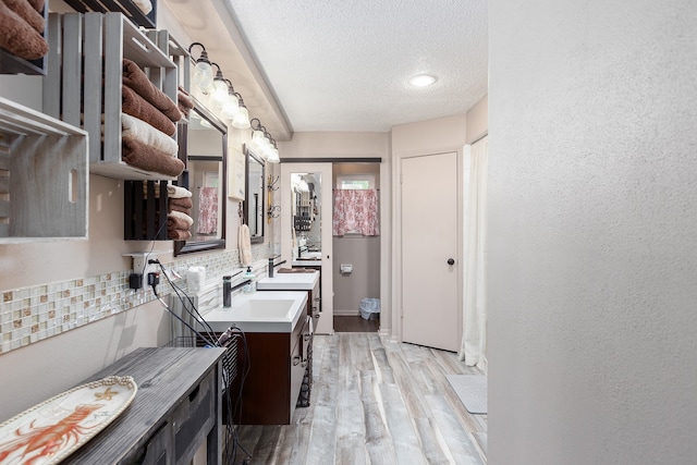 kitchen with decorative backsplash, sink, light wood-type flooring, and a textured ceiling