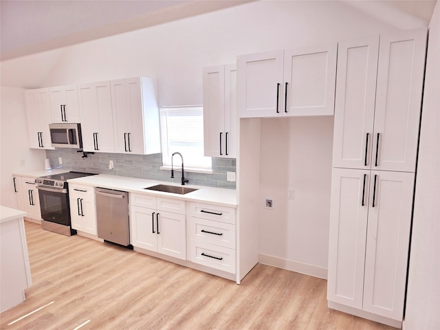 kitchen featuring vaulted ceiling, light hardwood / wood-style flooring, sink, stainless steel appliances, and white cabinets