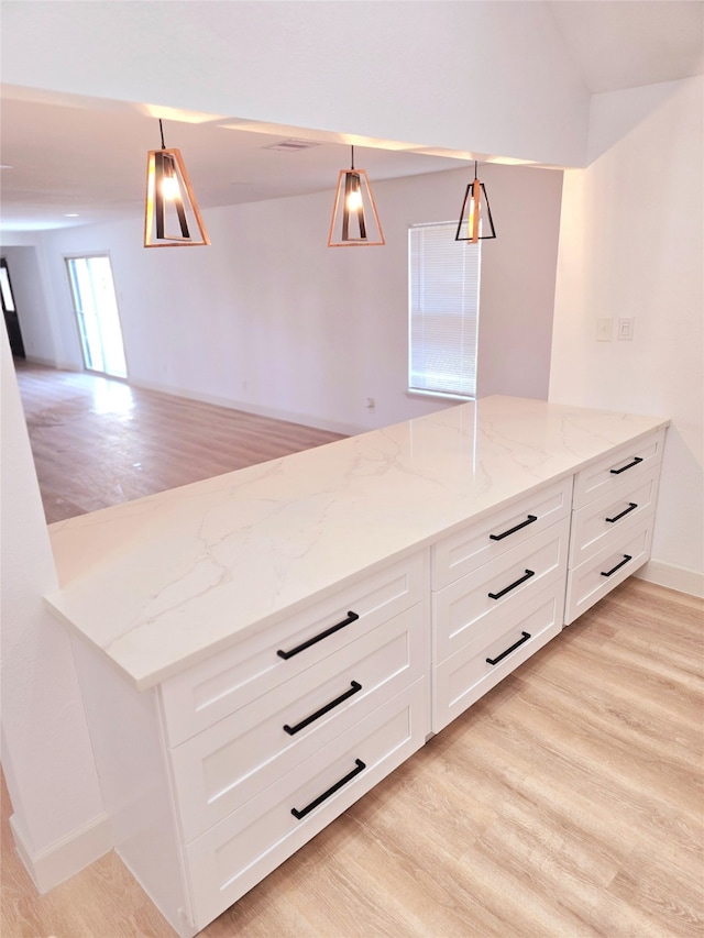 kitchen featuring decorative light fixtures, light hardwood / wood-style floors, light stone counters, and white cabinets