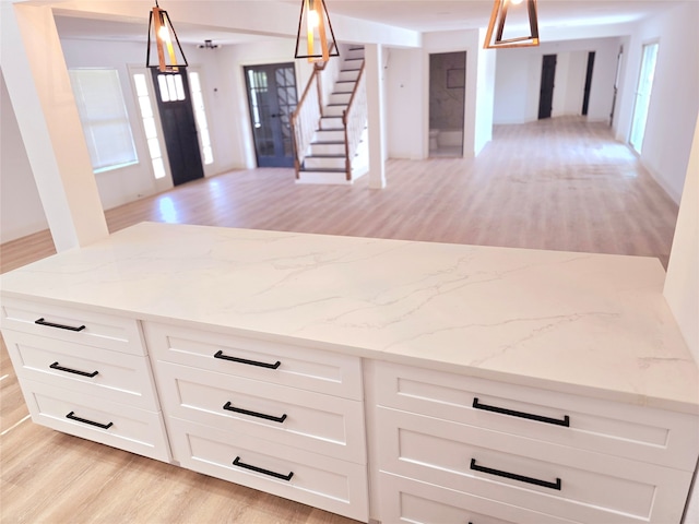 kitchen featuring light wood-type flooring, pendant lighting, white cabinets, and light stone counters