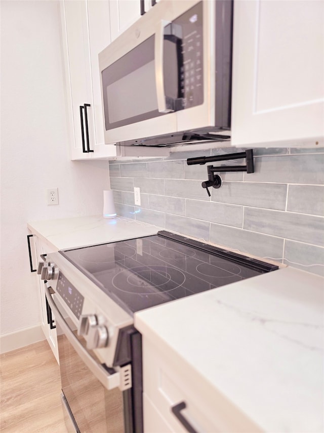 kitchen with stainless steel appliances, light stone countertops, light hardwood / wood-style floors, white cabinets, and decorative backsplash