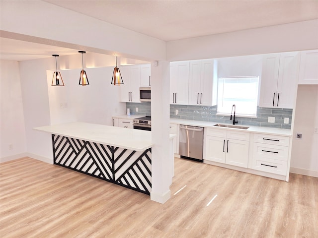 kitchen with appliances with stainless steel finishes, hanging light fixtures, light wood-type flooring, white cabinets, and sink