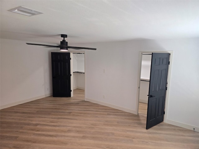 unfurnished bedroom with ceiling fan, light hardwood / wood-style flooring, a walk in closet, and a closet