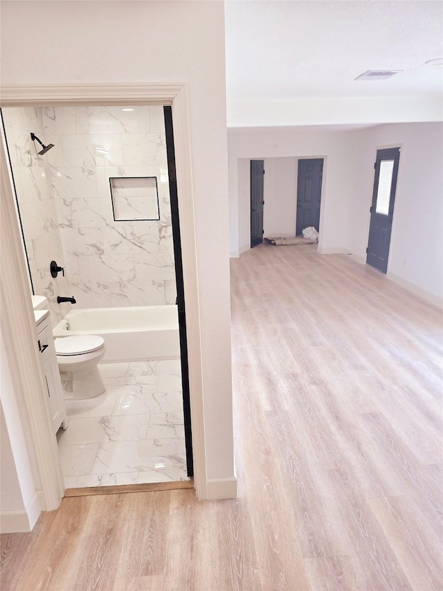 full bathroom with wood-type flooring, vanity, tiled shower / bath, and toilet