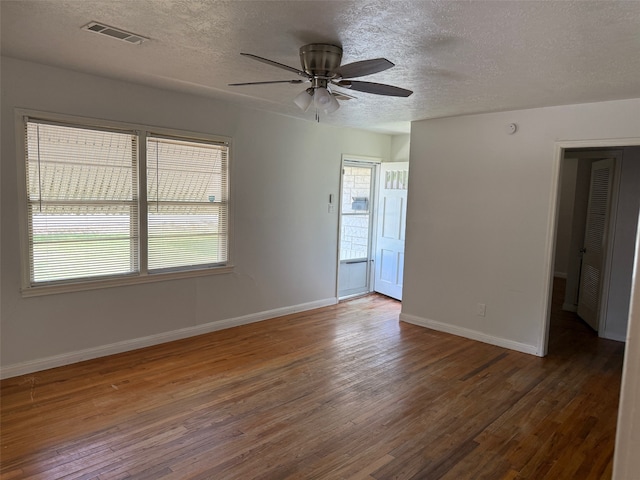 empty room with a wealth of natural light, a textured ceiling, and dark hardwood / wood-style floors