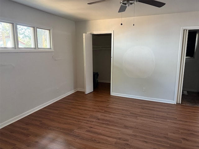 unfurnished bedroom with a closet, a spacious closet, ceiling fan, baseboards, and dark wood-type flooring