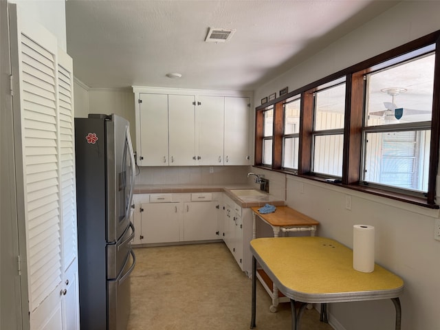 kitchen with white cabinets, a textured ceiling, stainless steel fridge, and sink