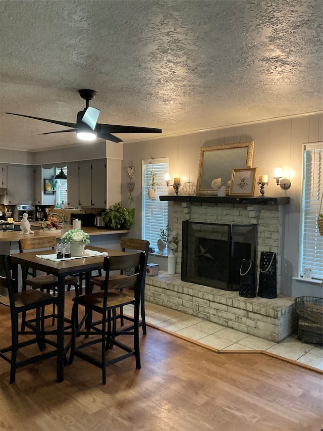 dining space with hardwood / wood-style floors, a brick fireplace, and ceiling fan