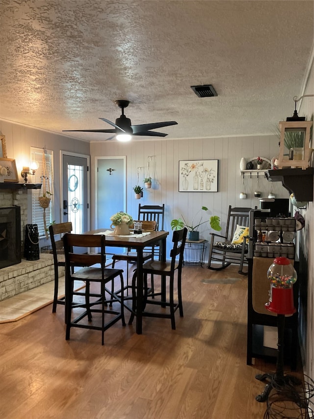 dining room featuring hardwood / wood-style flooring, a brick fireplace, a textured ceiling, and ceiling fan