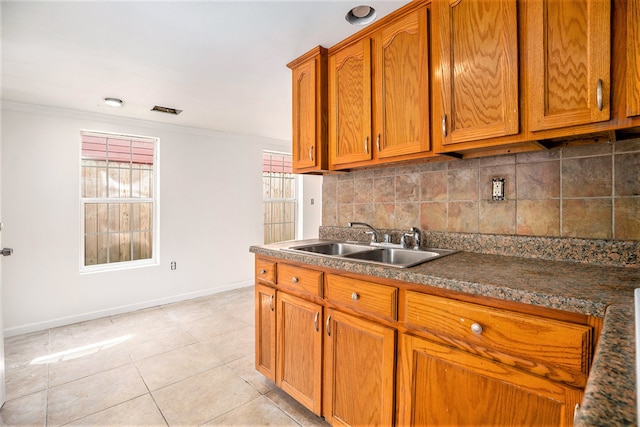 kitchen with light tile patterned flooring, sink, backsplash, crown molding, and dark stone countertops