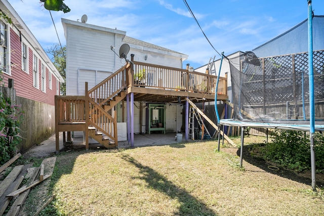 back of house featuring a trampoline, a deck, a lawn, and a patio area