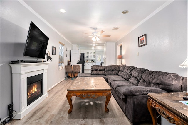 living room with ceiling fan, crown molding, and light hardwood / wood-style floors