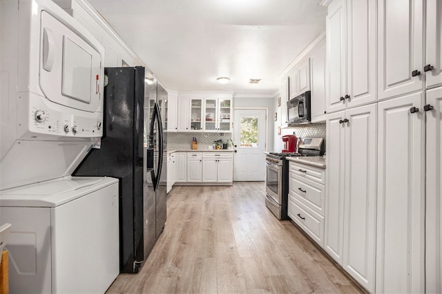 kitchen with stainless steel range with gas cooktop, white cabinetry, light wood-type flooring, stacked washer and dryer, and decorative backsplash