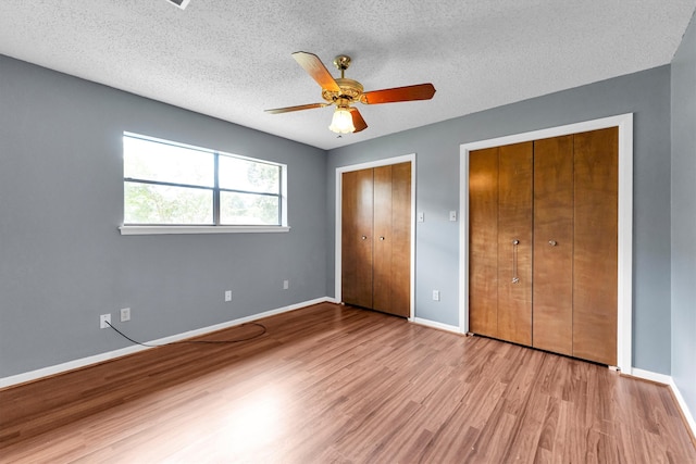 unfurnished bedroom with light wood-type flooring, multiple closets, ceiling fan, and a textured ceiling