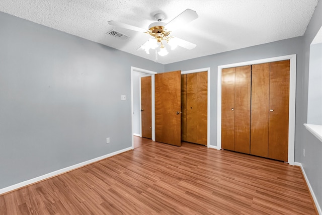 unfurnished bedroom with ceiling fan, multiple closets, a textured ceiling, and light wood-type flooring