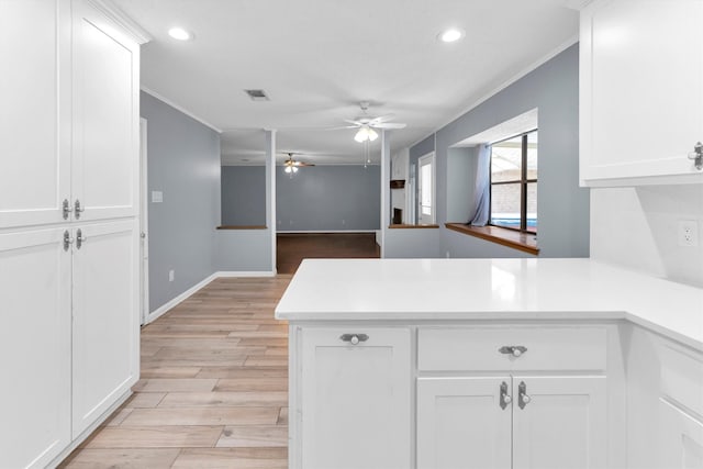 kitchen with light wood-type flooring, kitchen peninsula, ceiling fan, and white cabinets