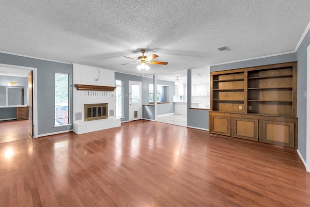 unfurnished living room with a fireplace, a textured ceiling, crown molding, ceiling fan, and hardwood / wood-style flooring