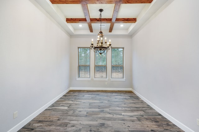 empty room with a notable chandelier, wood-type flooring, beam ceiling, and coffered ceiling