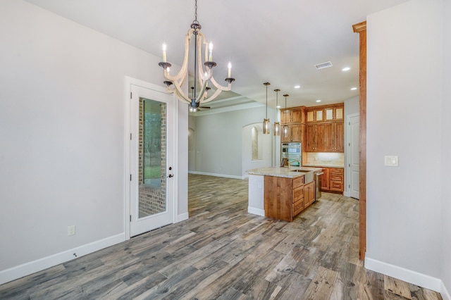 kitchen with an island with sink, hanging light fixtures, backsplash, a chandelier, and hardwood / wood-style flooring