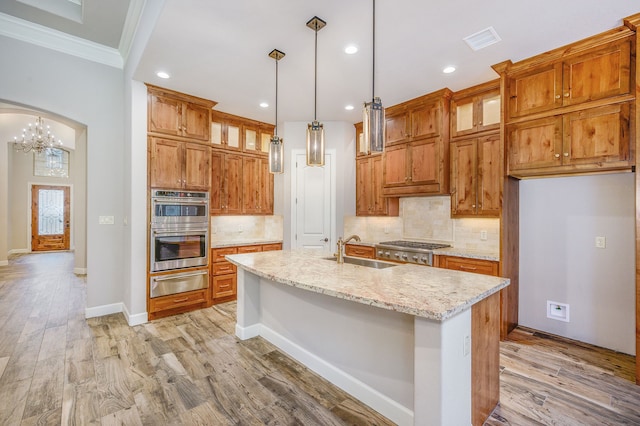 kitchen featuring sink, a kitchen island with sink, appliances with stainless steel finishes, an inviting chandelier, and light stone countertops