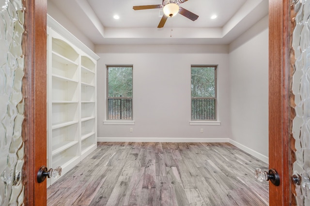 unfurnished room with light hardwood / wood-style flooring, a tray ceiling, ceiling fan, and plenty of natural light