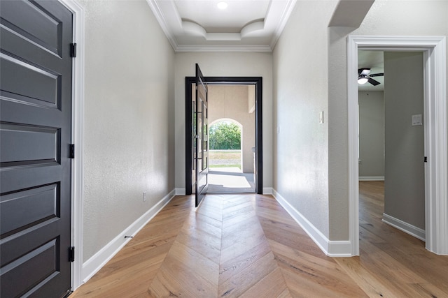 foyer entrance with light wood-type flooring, ceiling fan, a raised ceiling, and crown molding