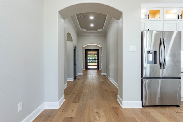 corridor with ornamental molding, light hardwood / wood-style floors, and a raised ceiling