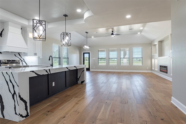 kitchen featuring hanging light fixtures, light hardwood / wood-style floors, light stone counters, white cabinets, and custom exhaust hood