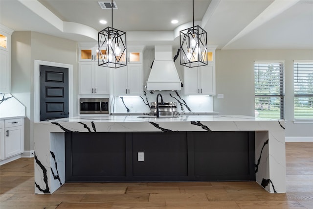 kitchen featuring a spacious island, light stone countertops, hanging light fixtures, and custom range hood