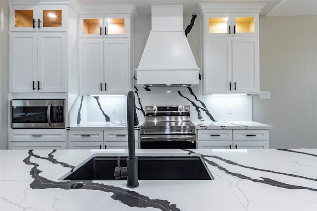 kitchen with stainless steel appliances, white cabinetry, light stone counters, and custom exhaust hood