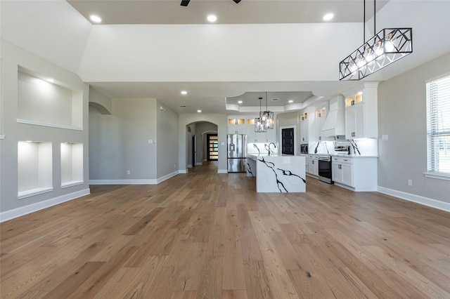 kitchen with custom range hood, hanging light fixtures, white cabinetry, and light hardwood / wood-style flooring