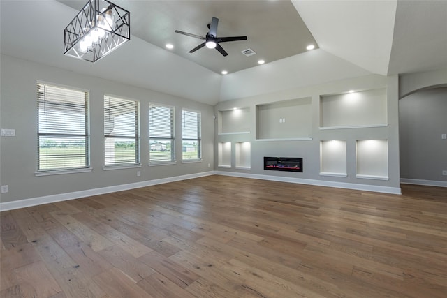 unfurnished living room with ceiling fan with notable chandelier, built in shelves, and hardwood / wood-style flooring