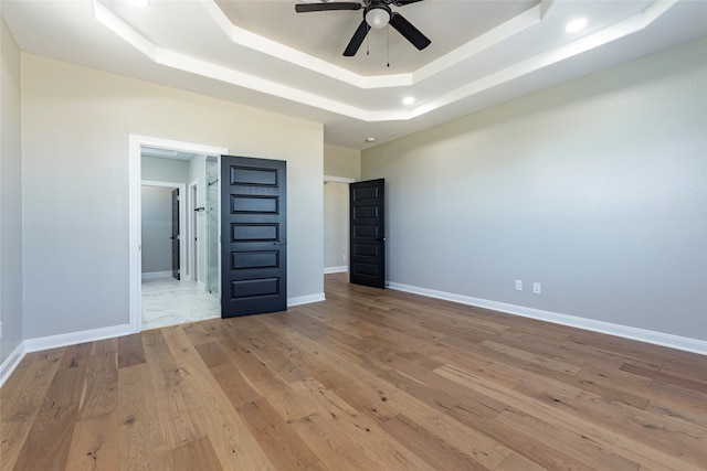 unfurnished bedroom featuring ceiling fan, a raised ceiling, and light hardwood / wood-style floors