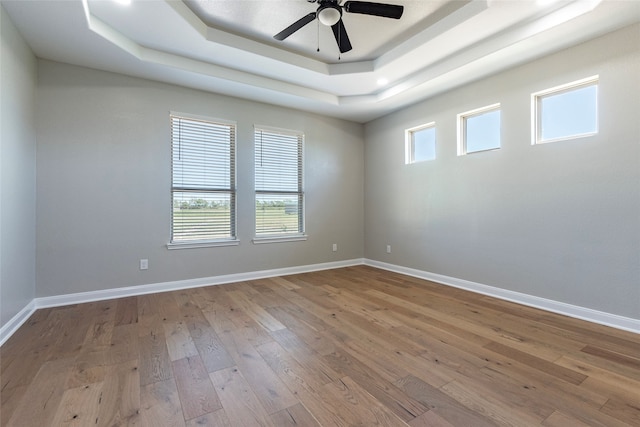 empty room featuring a tray ceiling, ceiling fan, and light hardwood / wood-style flooring