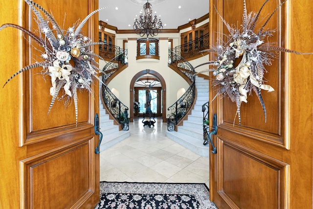 tiled entryway featuring crown molding, a chandelier, and a high ceiling