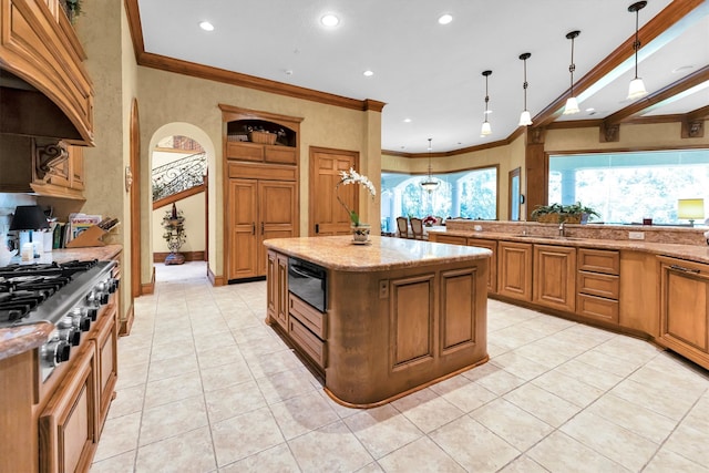 kitchen featuring light stone countertops, hanging light fixtures, ornamental molding, and a center island