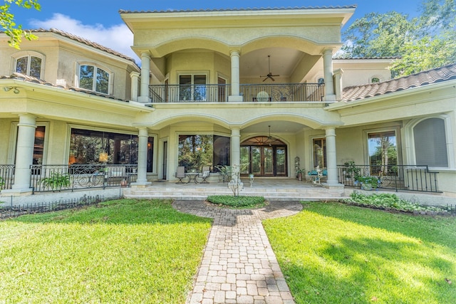 rear view of house with ceiling fan, a balcony, a porch, and a lawn