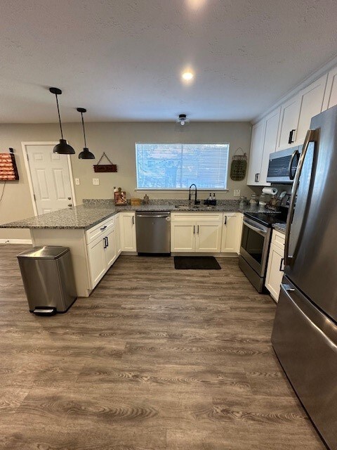 kitchen with pendant lighting, kitchen peninsula, appliances with stainless steel finishes, and white cabinets