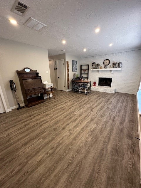 living room with a fireplace, dark wood-type flooring, a textured ceiling, and brick wall