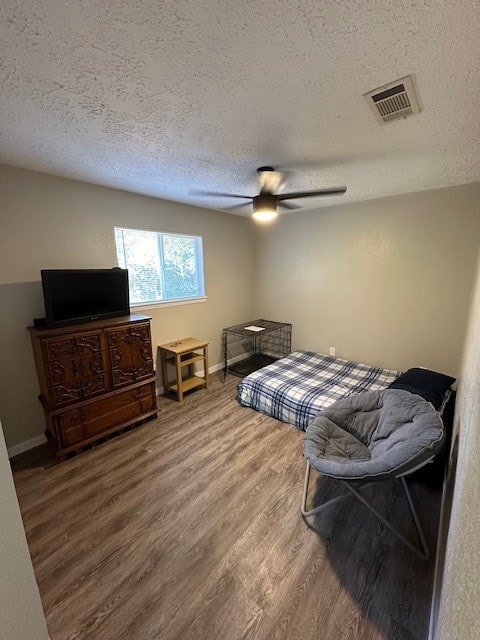 bedroom with hardwood / wood-style floors, ceiling fan, and a textured ceiling