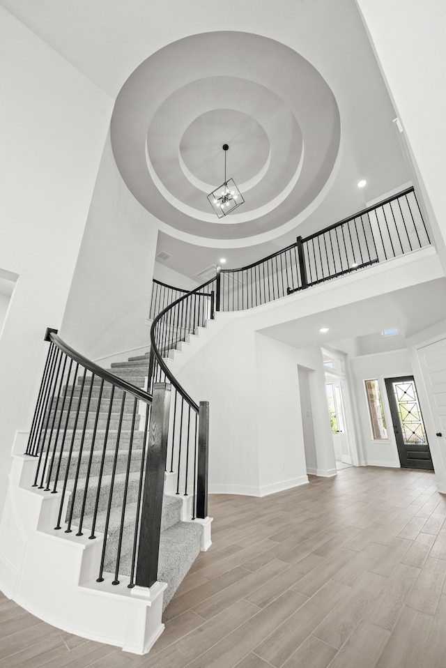 staircase featuring wood-type flooring, a raised ceiling, and a high ceiling