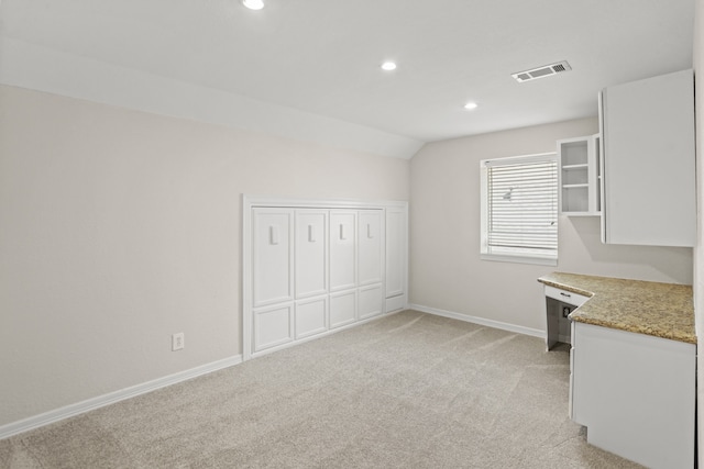 interior space with vaulted ceiling, light carpet, and white cabinets