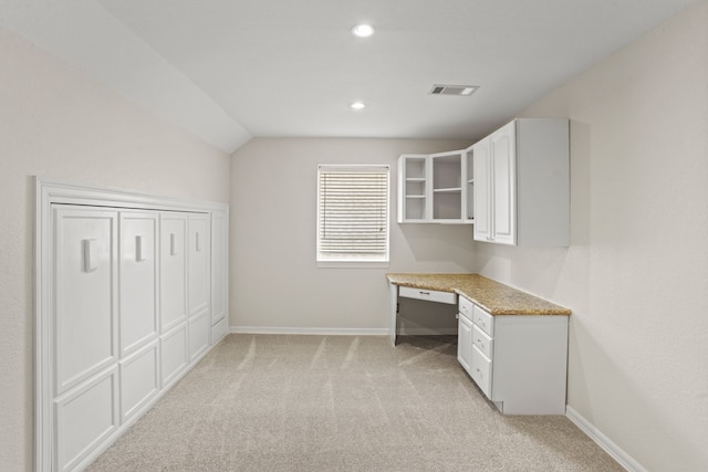 unfurnished office featuring light colored carpet, lofted ceiling, and built in desk