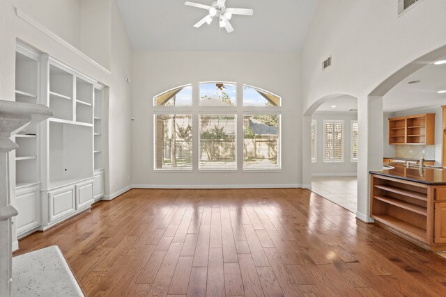 unfurnished living room with high vaulted ceiling, wood-type flooring, ceiling fan, and sink